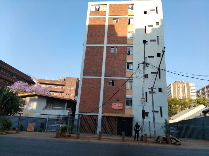 Front elevation of a multi-story apartment building featuring a brick and concrete facade with secure perimeter fencing and street-level access.