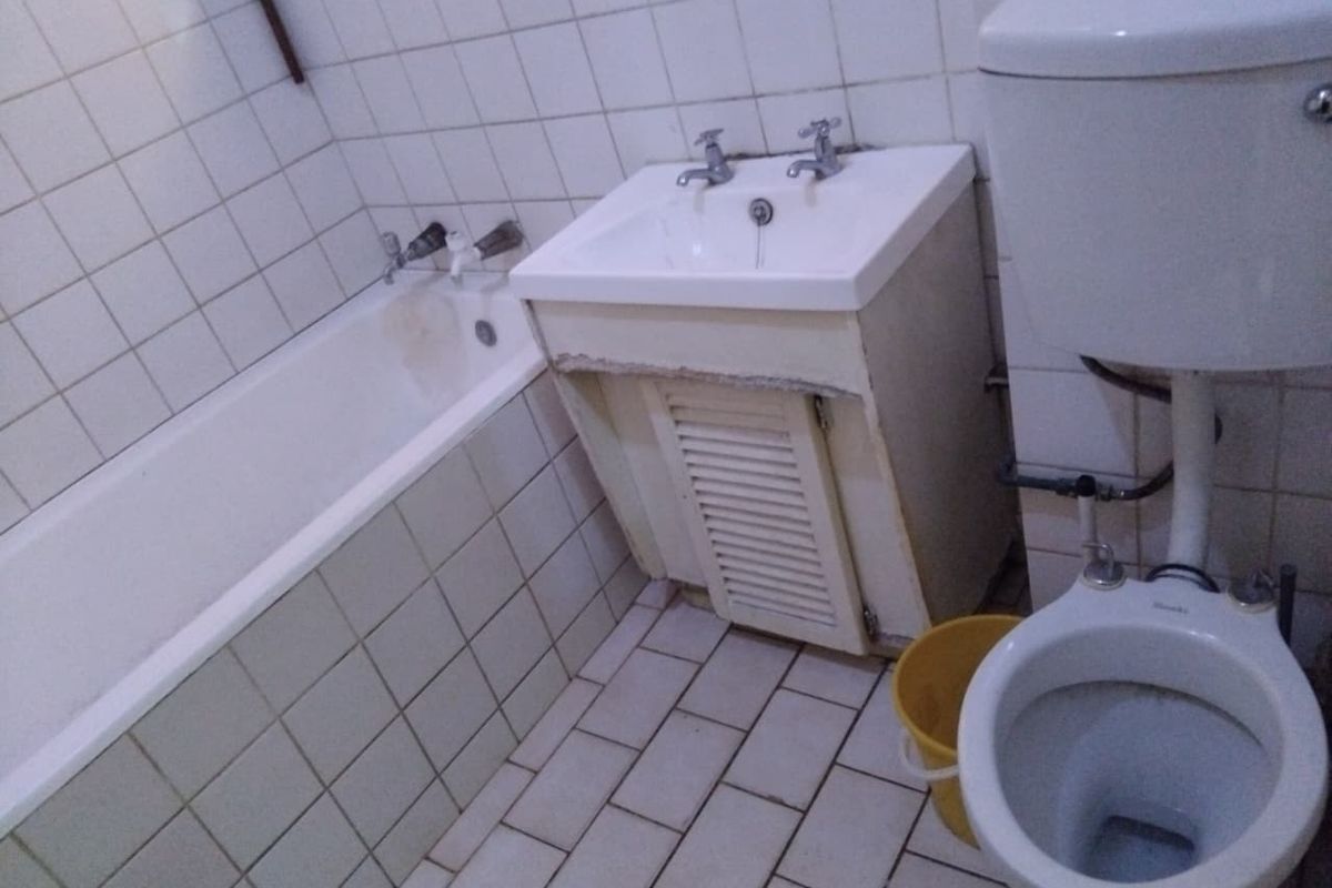 A dated bathroom featuring a bathtub, vanity basin, and toilet with tiled finishes, requiring renovation to update the worn fixtures and surfaces.