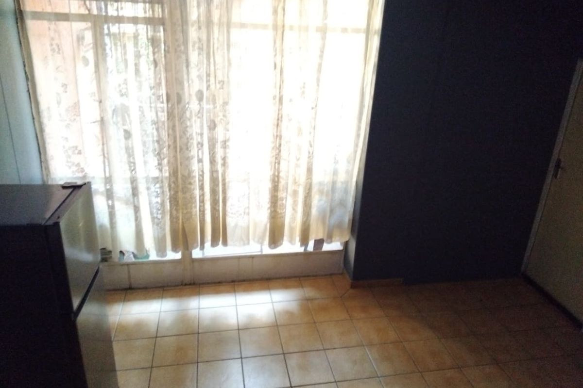 An empty living area featuring tiled flooring and a large window with sliding door access, providing natural light.