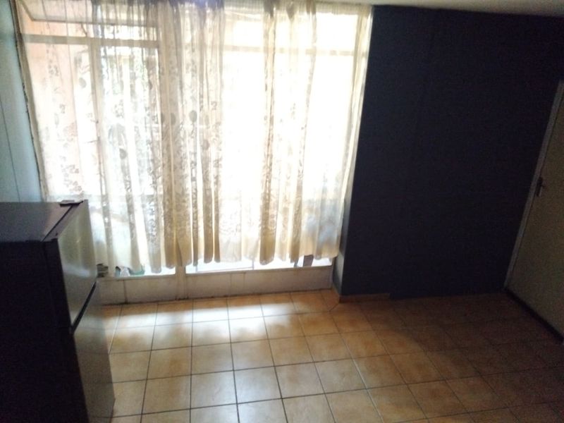 An empty living area featuring tiled flooring and a large window with sliding door access, providing natural light.