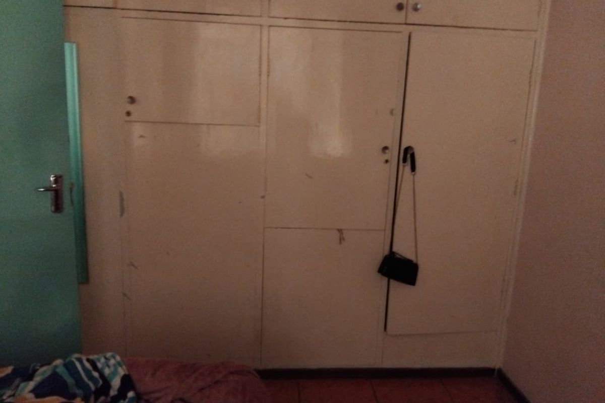 A bedroom featuring floor-to-ceiling built-in cupboards with tiled flooring, showing signs of wear and dated finishes.