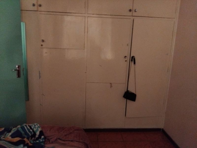 A bedroom featuring floor-to-ceiling built-in cupboards with tiled flooring, showing signs of wear and dated finishes.