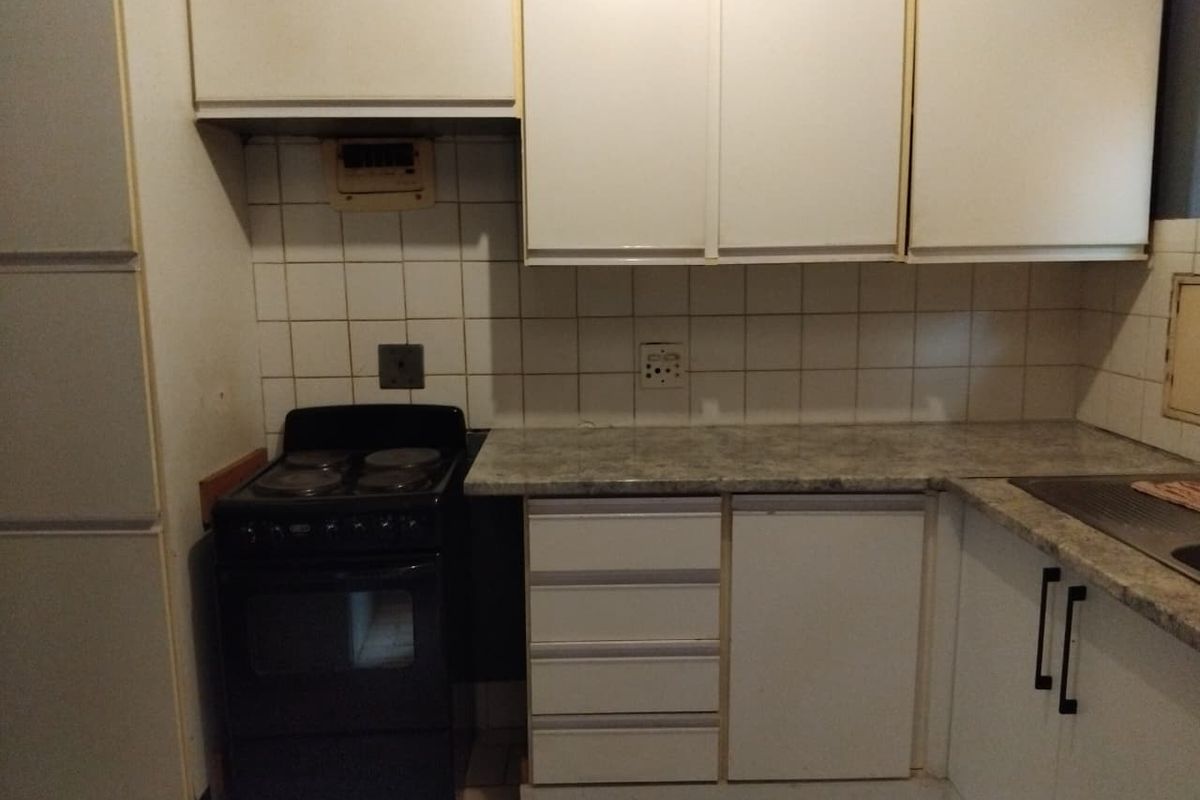 A dated kitchen featuring white cabinetry, laminate countertops, a tiled backsplash, and a freestanding electric stove, offering potential for modernization.