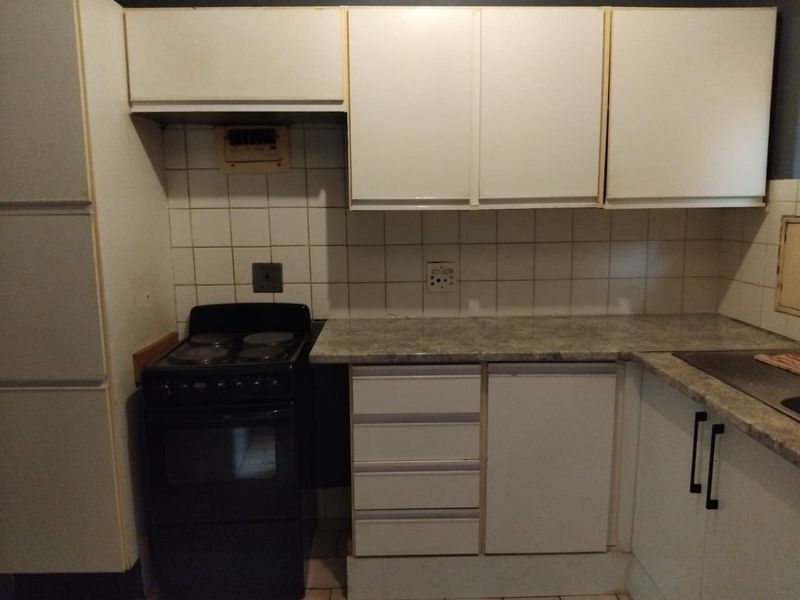 A dated kitchen featuring white cabinetry, laminate countertops, a tiled backsplash, and a freestanding electric stove, offering potential for modernization.