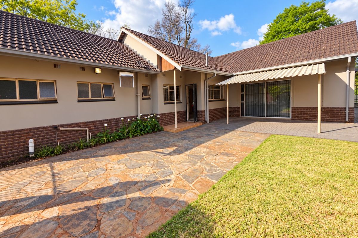 Rear exterior view featuring a paved patio area, covered awning, well-maintained lawn, and brick-accented facade with tiled roofing.