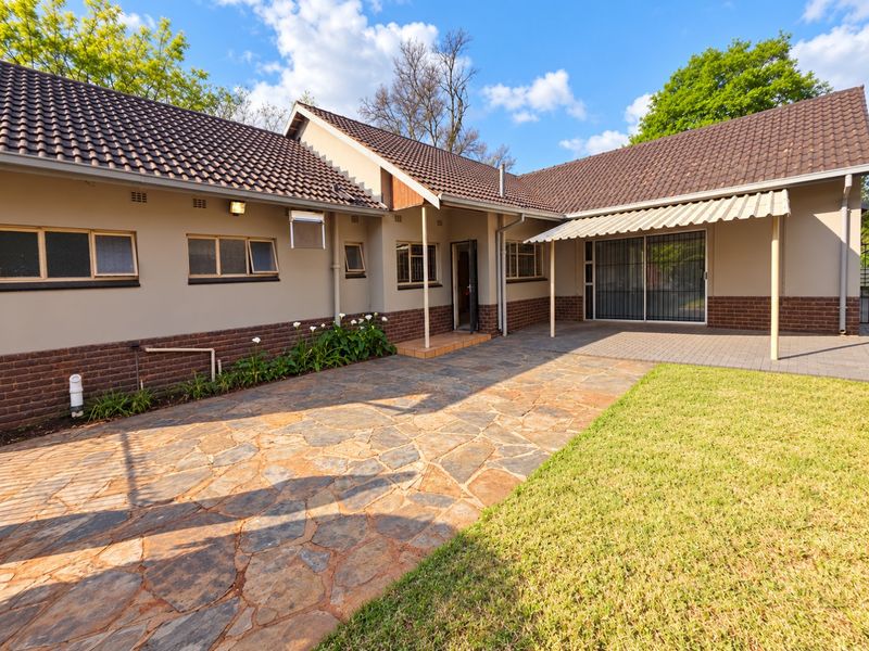 Rear exterior view featuring a paved patio area, covered awning, well-maintained lawn, and brick-accented facade with tiled roofing.