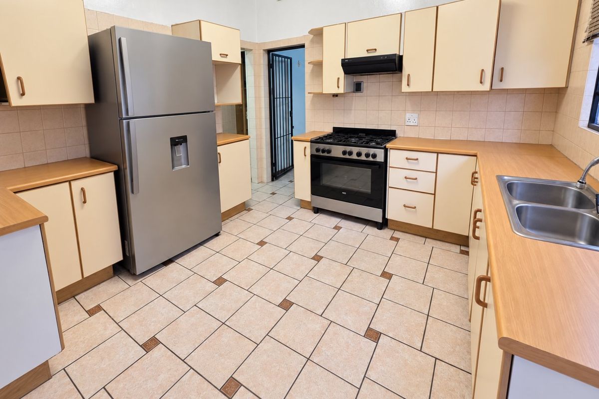 Functional kitchen featuring light-toned cabinetry, laminate countertops, a gas stove with extractor fan, and tiled flooring throughout.