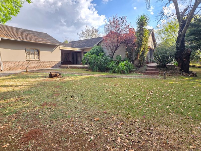 Rear view of the house featuring a tiled roof, brick facade, attached garage, and a spacious garden with mature trees and a paved walkway.