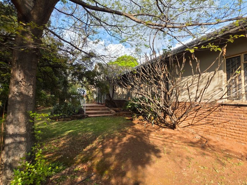 Rear view of the property featuring a brick facade, concrete steps, and established garden area with mature trees.