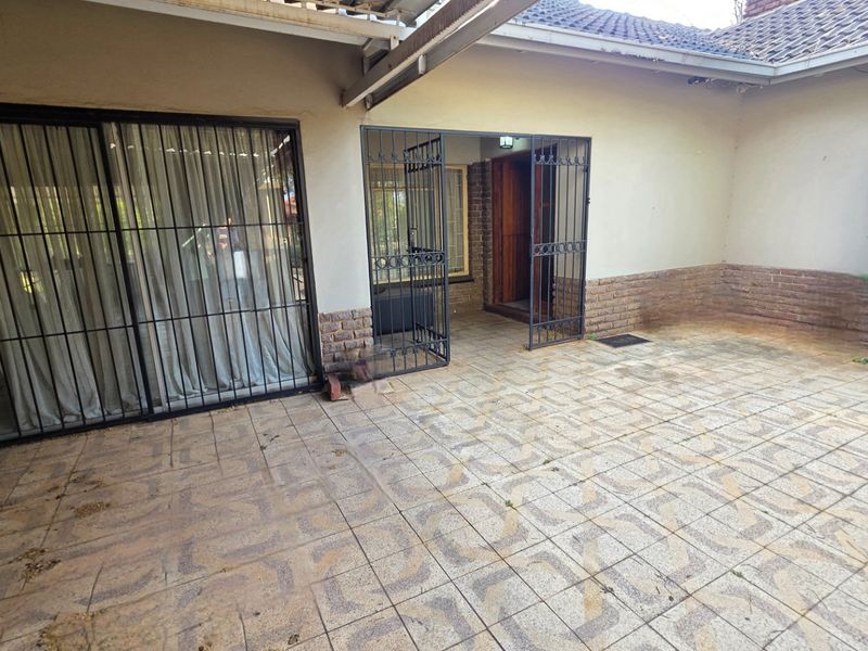 A covered outdoor patio area featuring tiled flooring, security gates, and access to the main house through sliding glass doors.