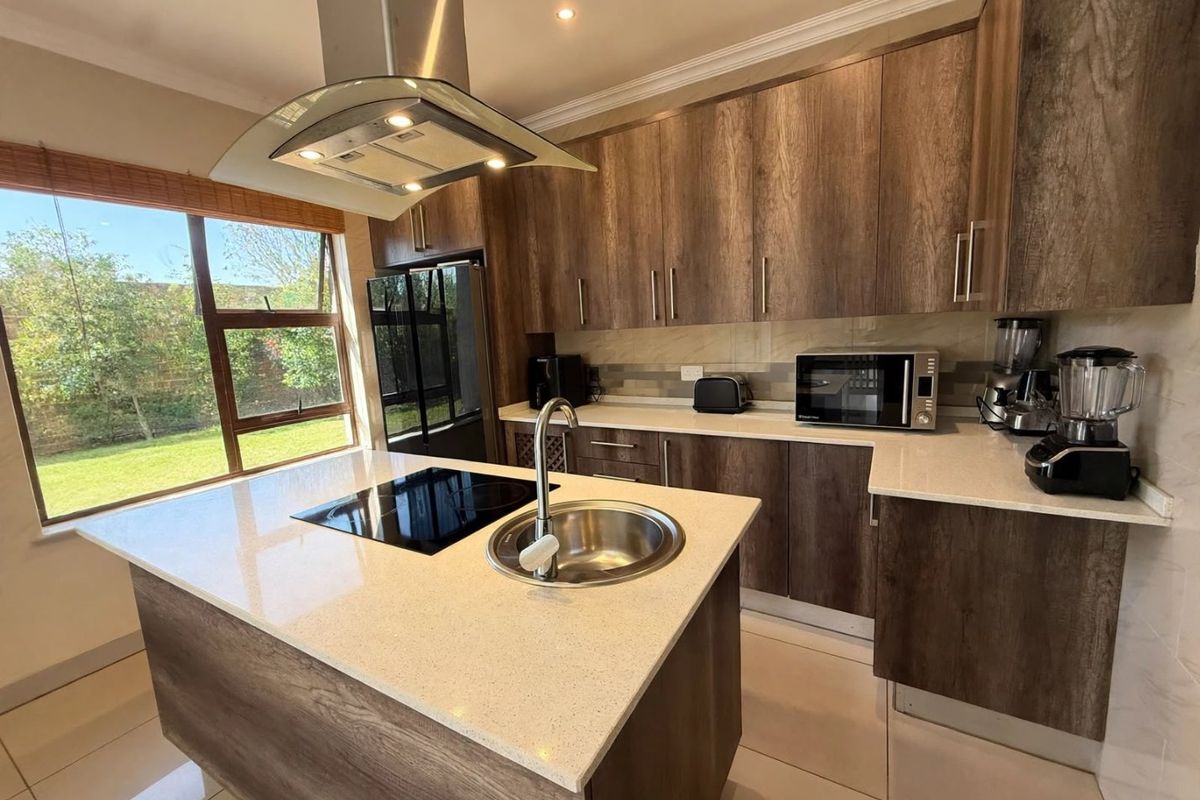 Modern kitchen featuring a central island with a built-in hob and sink, quartz countertops, and ample wood-finish cabinetry with integrated lighting.