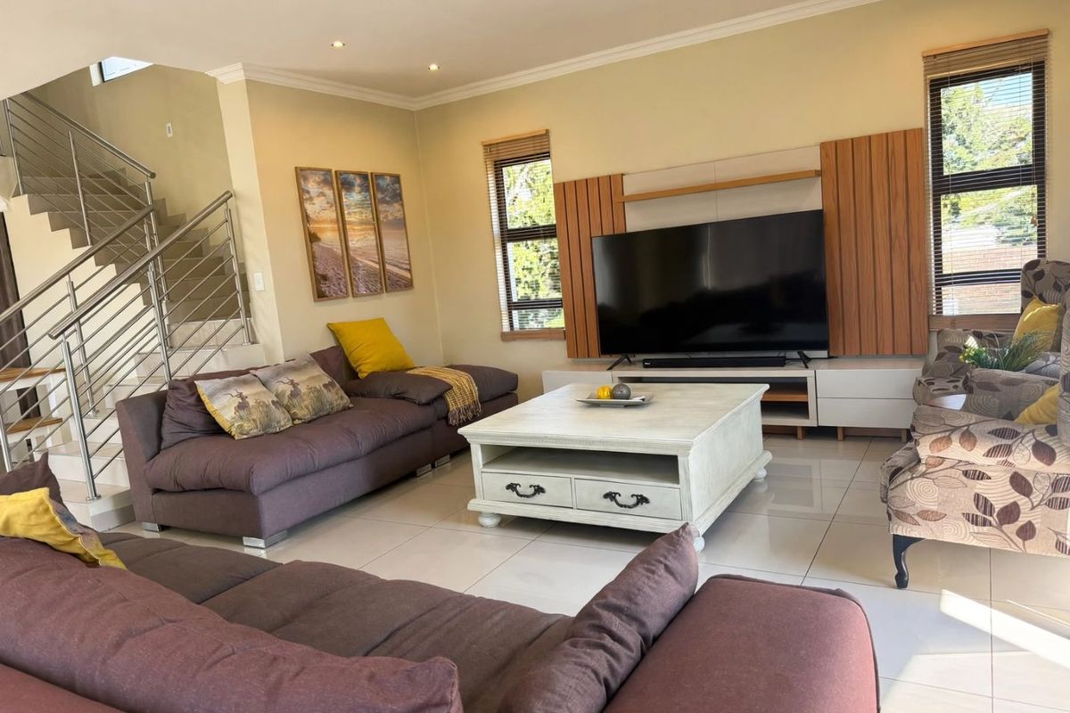 Spacious living room featuring tiled flooring, a modern staircase with stainless steel balustrades, and a custom built-in media unit.