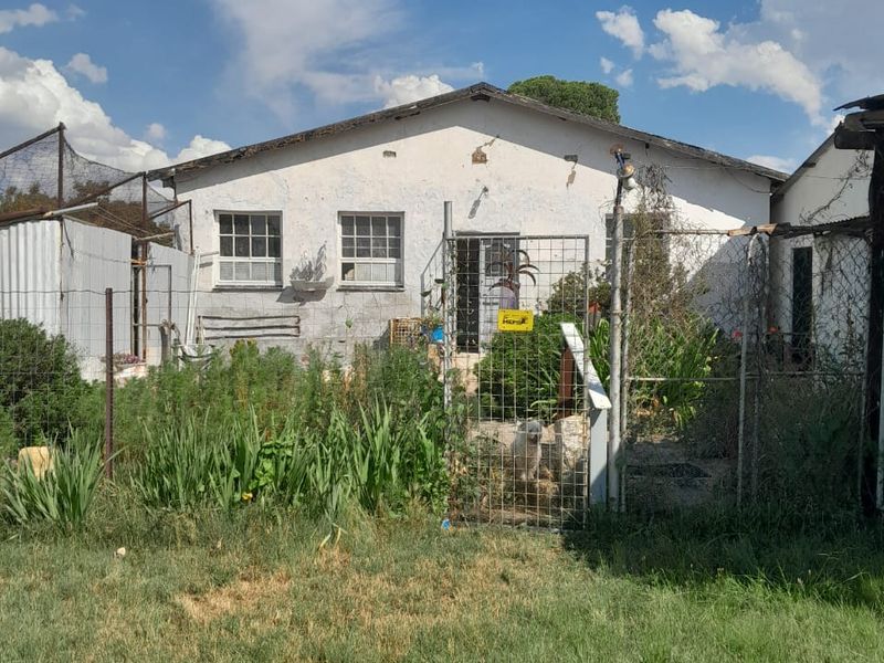 Rear view of a detached house featuring a gabled roof, security fencing, and a garden area requiring maintenance.