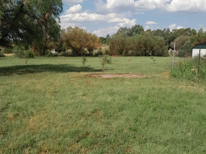 A spacious, open grass garden area featuring mature trees and perimeter fencing, offering a blank canvas for landscaping potential.