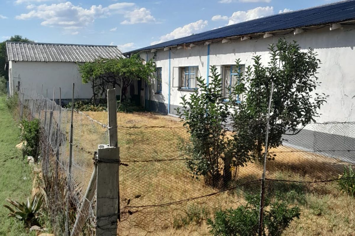 Rear view of the property featuring a long building structure with corrugated metal roofing, enclosed by a wire mesh fence and concrete posts.
