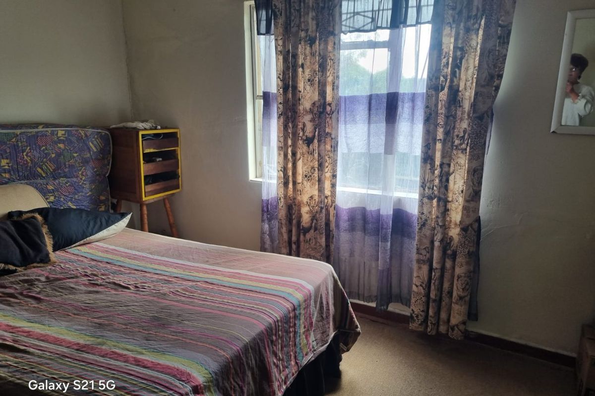A bedroom featuring carpeted flooring and a window with curtains. The room shows signs of wear on the walls and requires cosmetic updates.