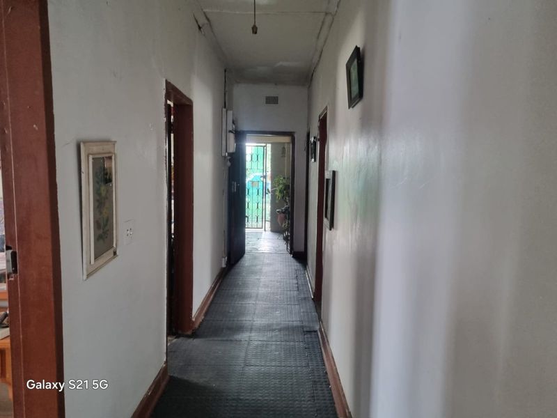A narrow residential hallway featuring dark flooring and plain walls, leading towards an exterior doorway with security gate.