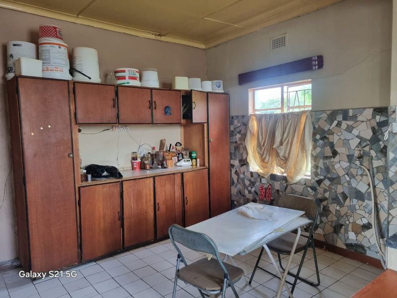 A dated kitchen featuring built-in wooden cabinetry, mosaic wall tiles, and tiled flooring, requiring modernization to improve functionality and aesthetic appeal.