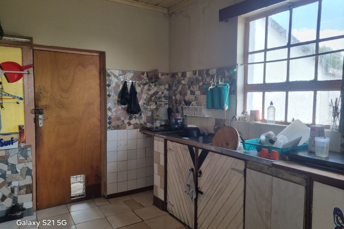 A dated kitchen area featuring original cabinetry, tiled splashbacks, and a grid window, requiring modernization and renovation to improve functionality and aesthetic appeal.