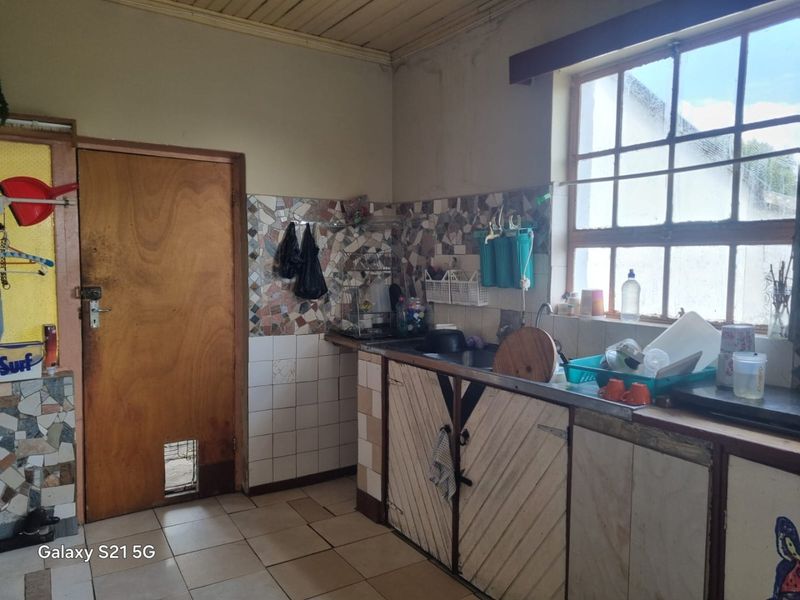 A dated kitchen area featuring original cabinetry, tiled splashbacks, and a grid window, requiring modernization and renovation to improve functionality and aesthetic appeal.