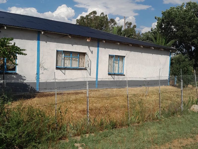 Rear view of a single-story house featuring a corrugated metal roof, steel-framed windows, and a wire mesh perimeter fence.
