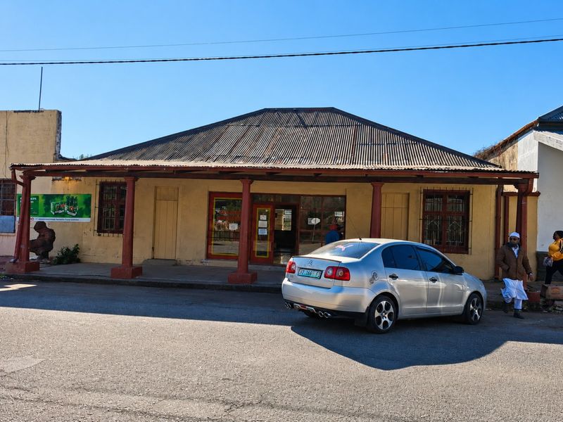 Front elevation of a commercial building featuring a covered veranda, corrugated iron roof, and security-barred windows, situated along a street frontage.