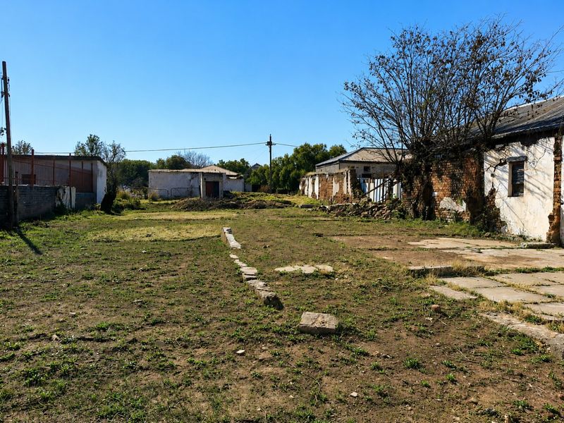 Expansive rear exterior area featuring weathered brick structures, boundary walls, and open ground, requiring significant maintenance or redevelopment.