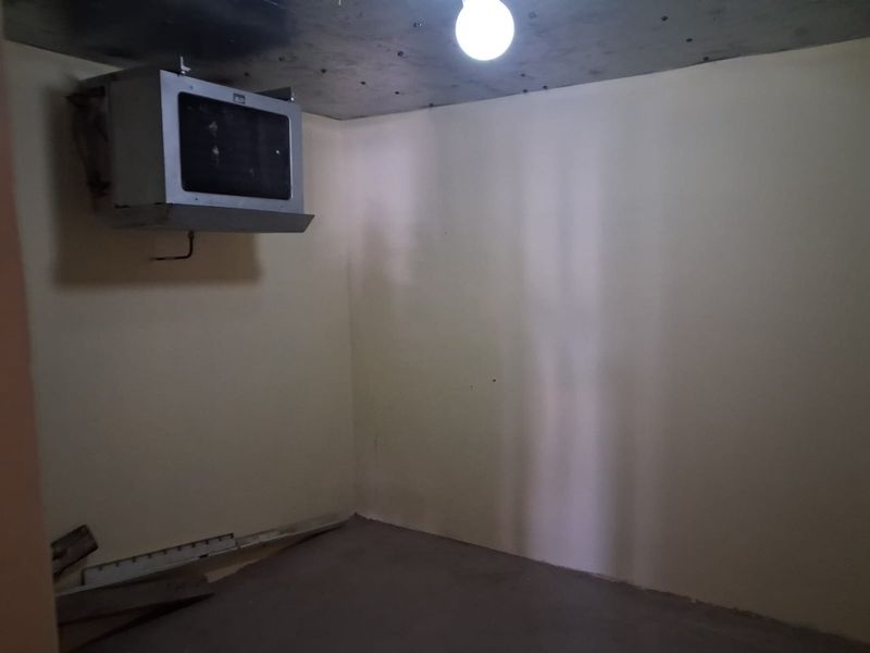 An unfinished utility space featuring a wall-mounted HVAC unit, exposed concrete ceiling, and basic lighting, suitable for storage or technical infrastructure.