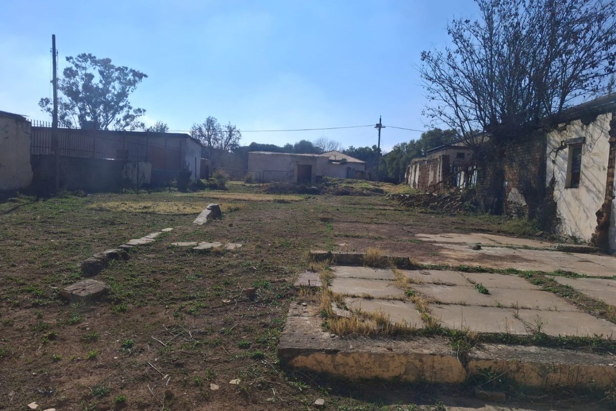 Expansive rear outdoor area featuring weathered outbuildings, concrete paving, and perimeter walls, offering significant potential for redevelopment or landscaping.