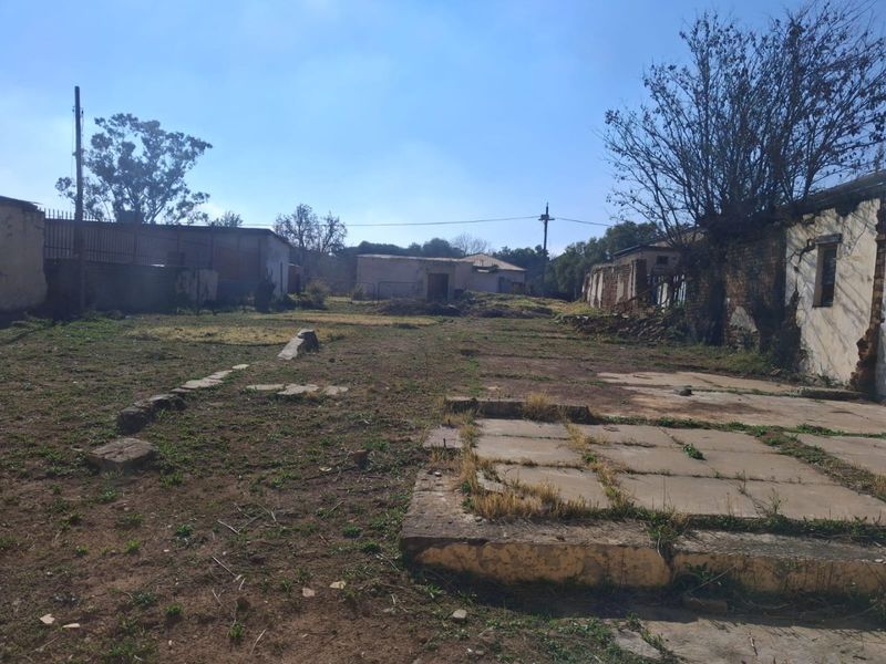 Expansive rear outdoor area featuring weathered outbuildings, concrete paving, and perimeter walls, offering significant potential for redevelopment or landscaping.