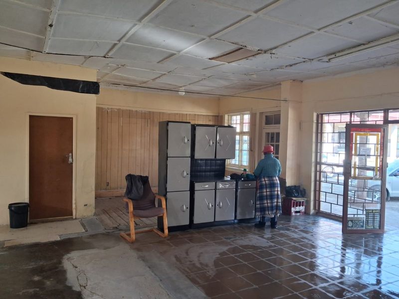Open-plan commercial space featuring tiled flooring, suspended ceiling, and security gate access, currently requiring significant maintenance and cosmetic refurbishment.