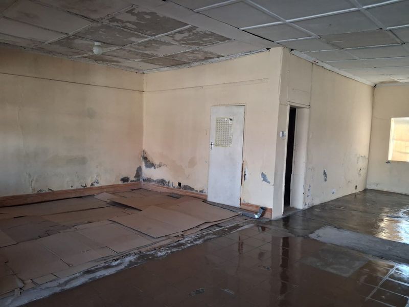 An empty, open-plan commercial space requiring significant renovation, featuring damaged ceiling tiles, peeling wall paint, and worn flooring.