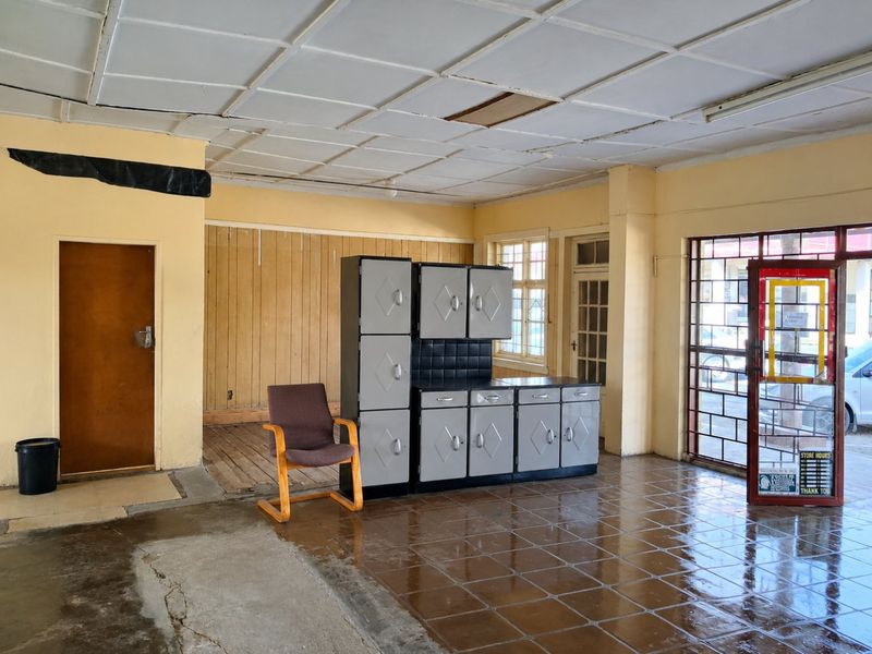 Open plan commercial space featuring tiled flooring, suspended ceiling, and security gate access, currently in need of renovation and repair.