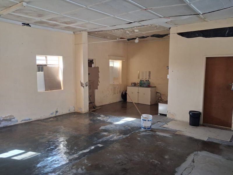An open-plan commercial space featuring concrete flooring, a suspended ceiling, and built-in cabinetry, currently in need of significant renovation and repair.