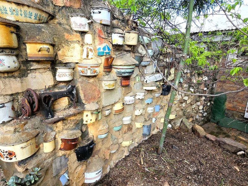 A rustic garden area featuring a stone wall decorated with vintage enamel pots and a built-in antique sewing machine base.