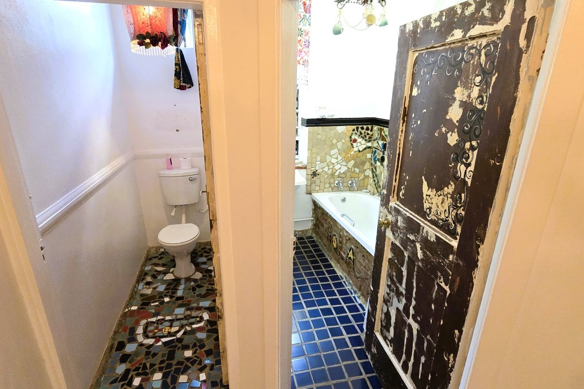 A bathroom featuring a separate toilet area with mosaic flooring and a main bathroom area with a built-in bathtub and blue tiled flooring.