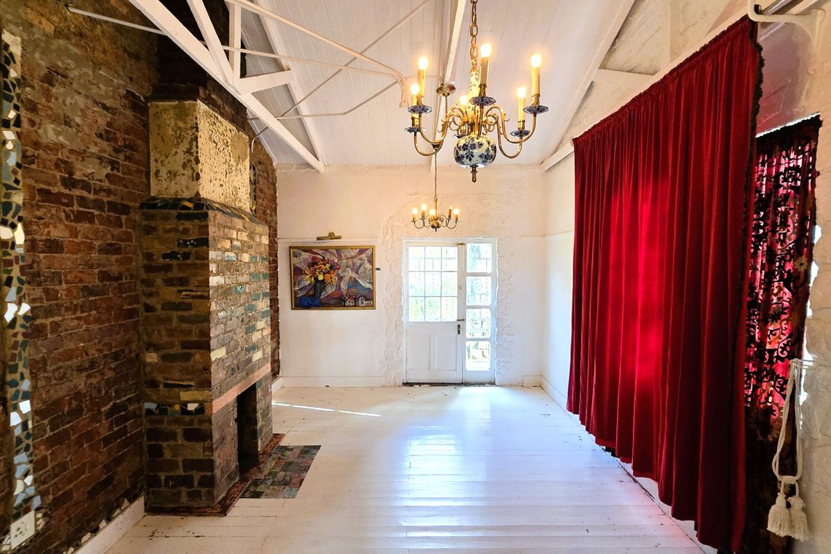 Spacious living area featuring exposed brick fireplace, high vaulted ceilings with timber trusses, and white painted timber flooring.