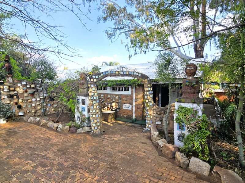 A unique front entrance featuring a decorative stone archway, brick paving, and extensive stone masonry walls set within a mature garden landscape.