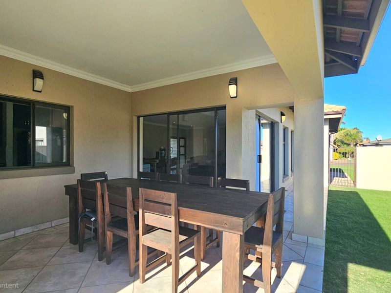 A covered outdoor patio area featuring tiled flooring, wall-mounted lighting, and sliding glass door access to the interior living space.