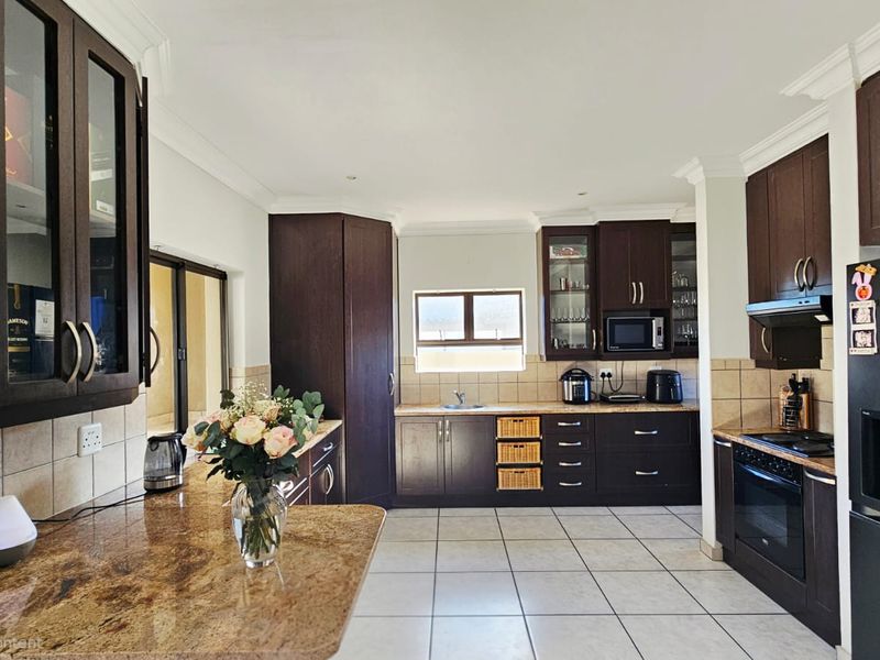 Spacious kitchen featuring dark wood cabinetry, granite countertops, tiled flooring, and integrated appliances, offering a functional and well-maintained cooking space.