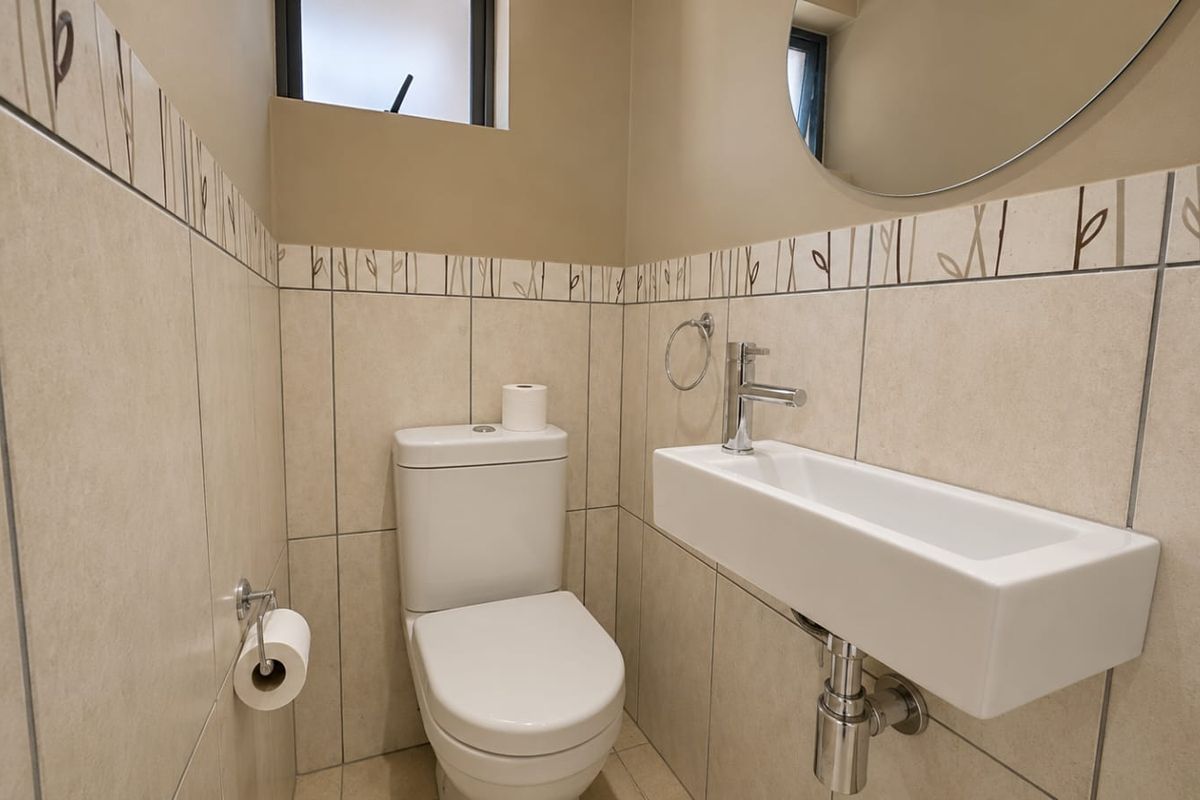 A compact, modern guest bathroom featuring neutral ceramic wall tiles, a wall-mounted basin with chrome fixtures, and a dual-flush toilet.