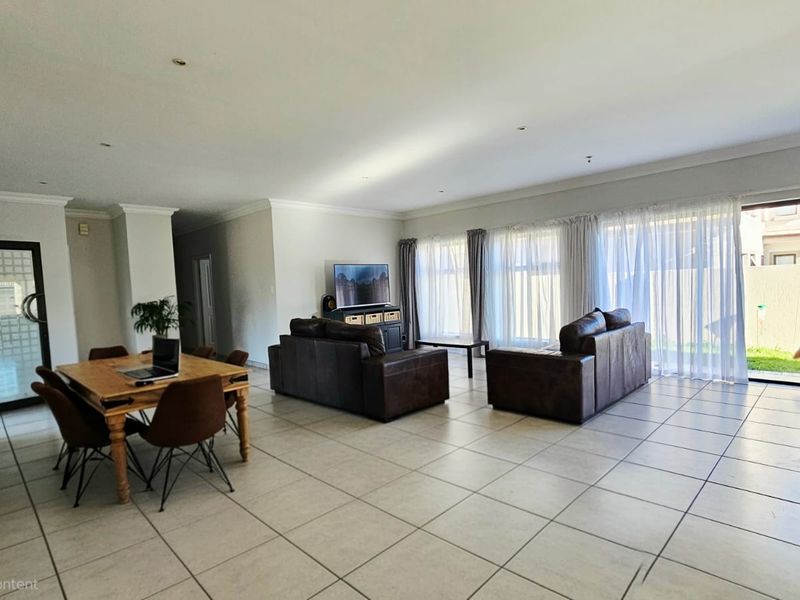 Spacious open-plan living and dining area featuring neutral tiled flooring, recessed lighting, and large sliding glass doors providing access to the garden.