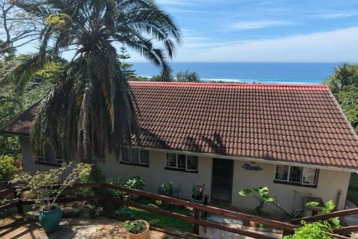 Rear view of the house featuring a tiled roof, timber deck railing, and scenic ocean views surrounded by lush greenery.