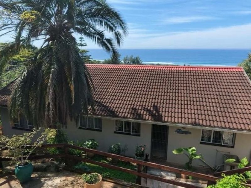 Rear view of the house featuring a tiled roof, timber deck railing, and scenic ocean views surrounded by lush greenery.