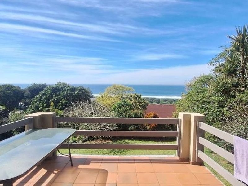 A spacious outdoor balcony featuring tiled flooring and a timber balustrade, offering expansive views of the surrounding landscape and ocean.