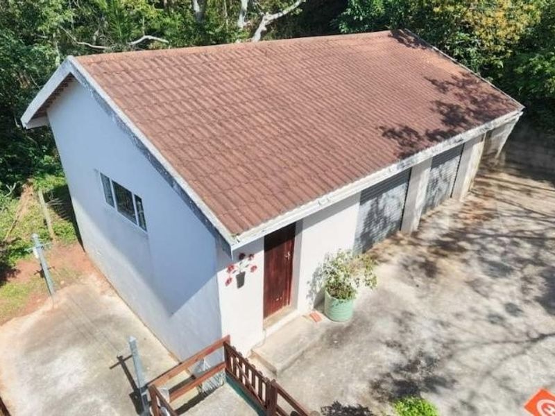 An elevated view of a detached double garage featuring a tiled roof and concrete driveway, situated in a lush, wooded setting.