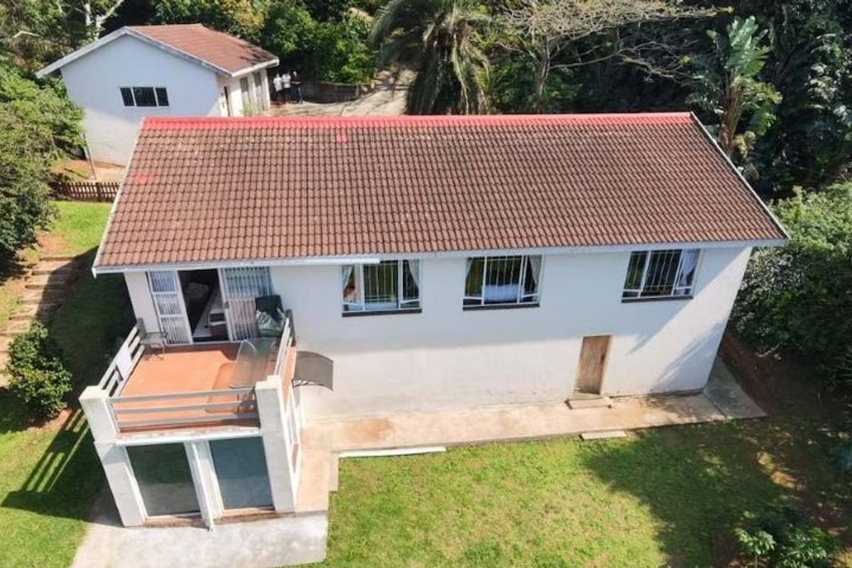 Aerial view of a residential property featuring a tiled roof, a raised balcony, and a detached outbuilding set within a garden environment.