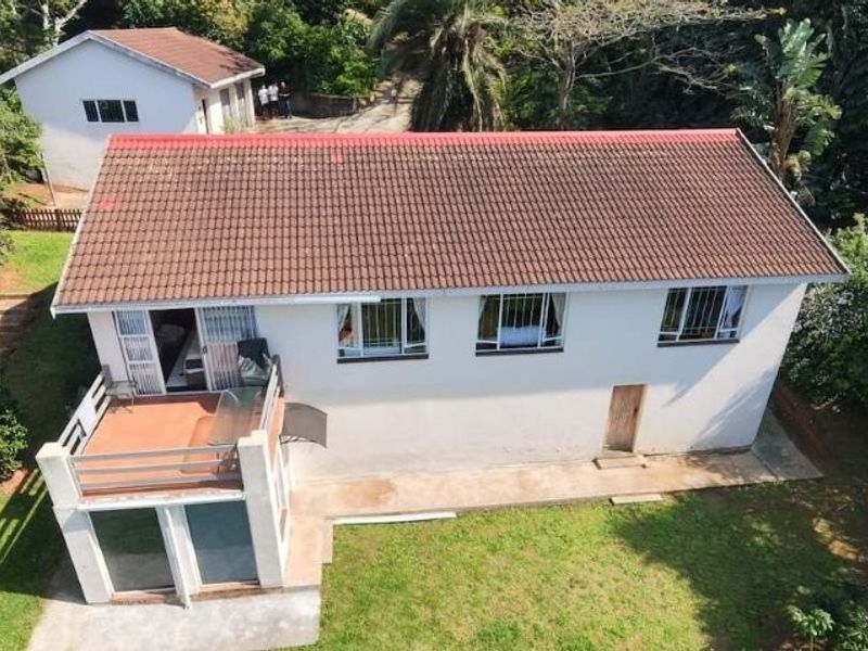 Aerial view of a residential property featuring a tiled roof, a raised balcony, and a detached outbuilding set within a garden environment.