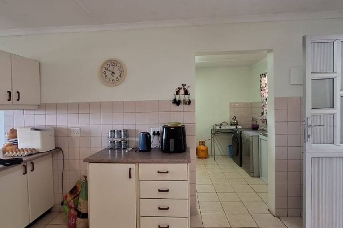A functional kitchen featuring built-in cabinetry, laminate countertops, and ceramic tiling, with an adjacent scullery area visible through the doorway.