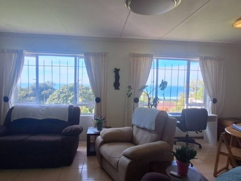 A living room featuring tiled flooring, large windows with security bars, and views of the ocean.